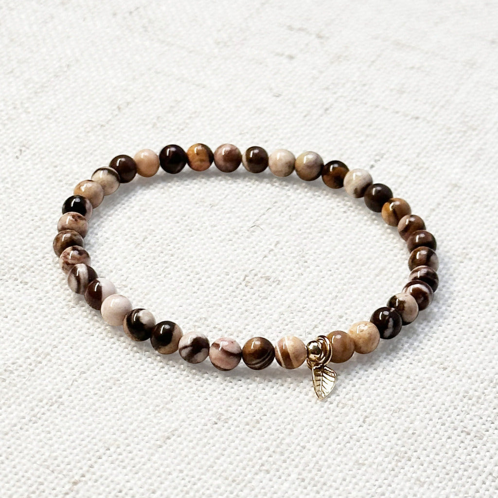 4mm zebra jasper bracelet with golden leaf charm resting on a neutral fabric