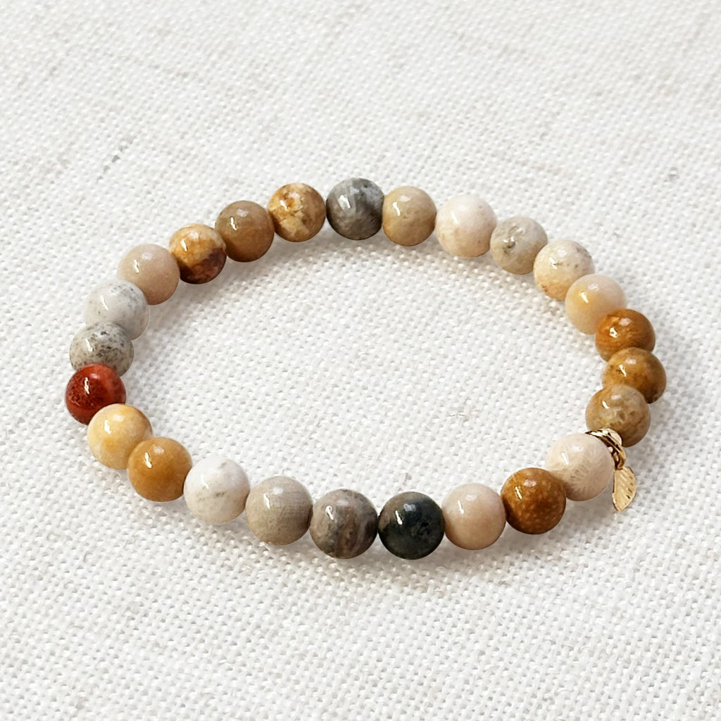 Coral jade bracelet with golden charm on linen background for heart chakra support