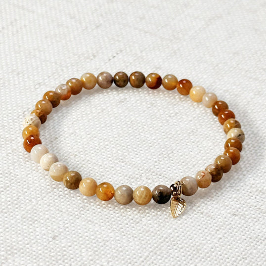 Close-up of coral jade crystal bracelet styled with soft-toned fabric