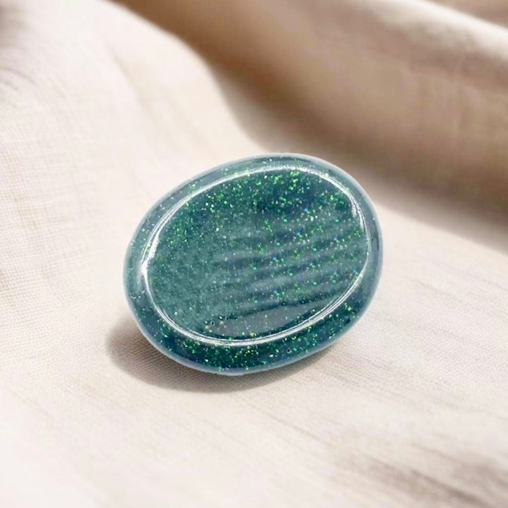 Thumb-shaped Green Goldstone worry stone, known for its sparkling surface, promoting confidence, stress relief, and emotional balance