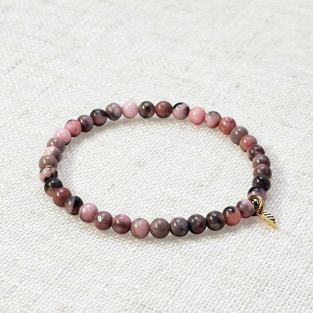 Pink zebra jasper bracelet with golden leaf charm on soft linen