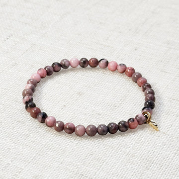 Pink zebra jasper bracelet with golden leaf charm on soft linen