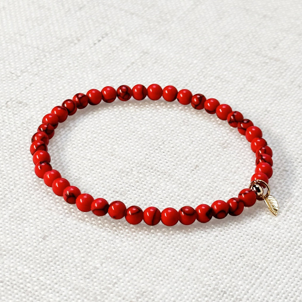 Red turquoise bracelet with 4mm beads and golden leaf charm on neutral background