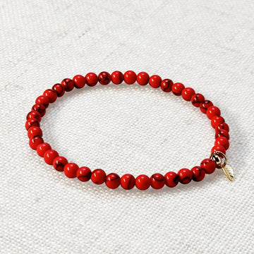 Red turquoise bracelet with 4mm beads and golden leaf charm on neutral background