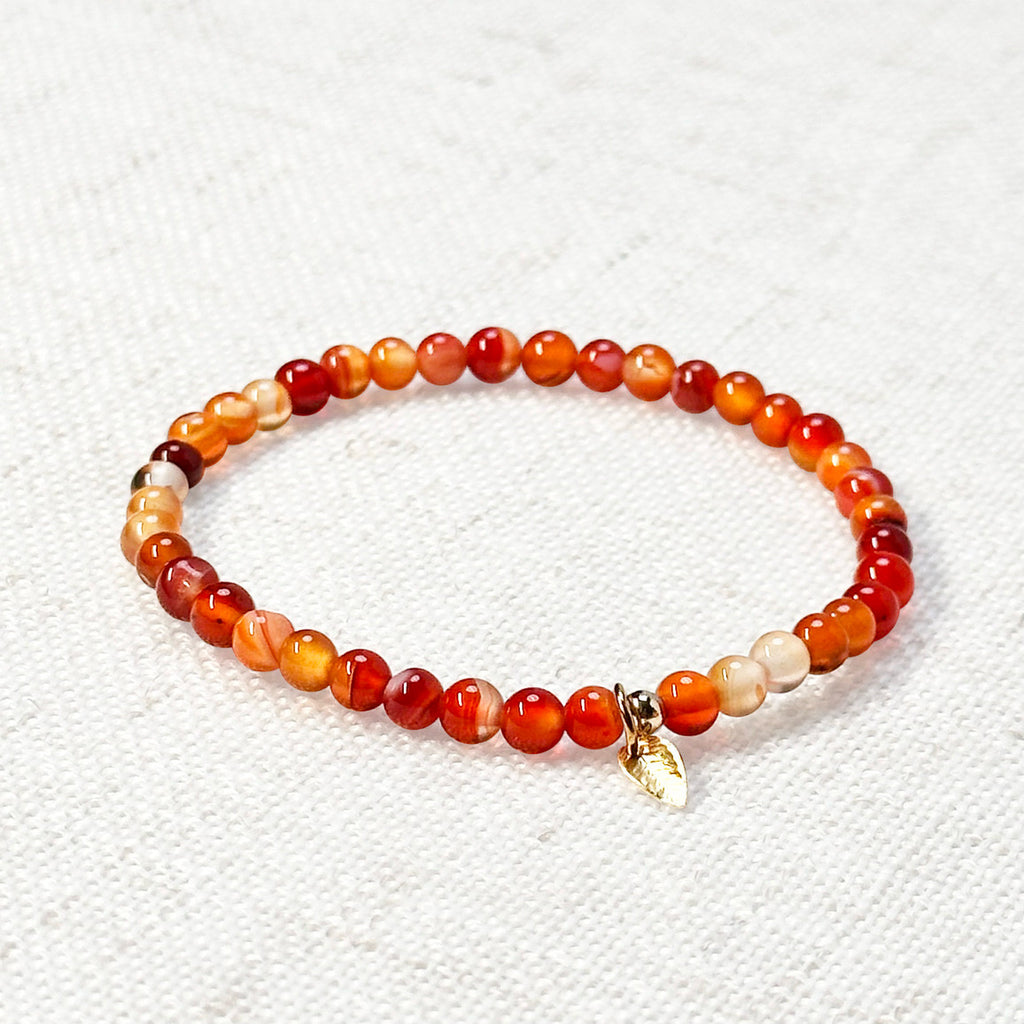 Sardonyx bracelet with golden leaf charm resting on linen
