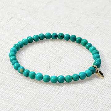 Turquoise bracelet with 4mm beads and golden leaf charm on neutral background