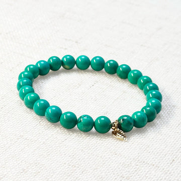 Turquoise bracelet with 6mm beads and golden leaf charm on white background