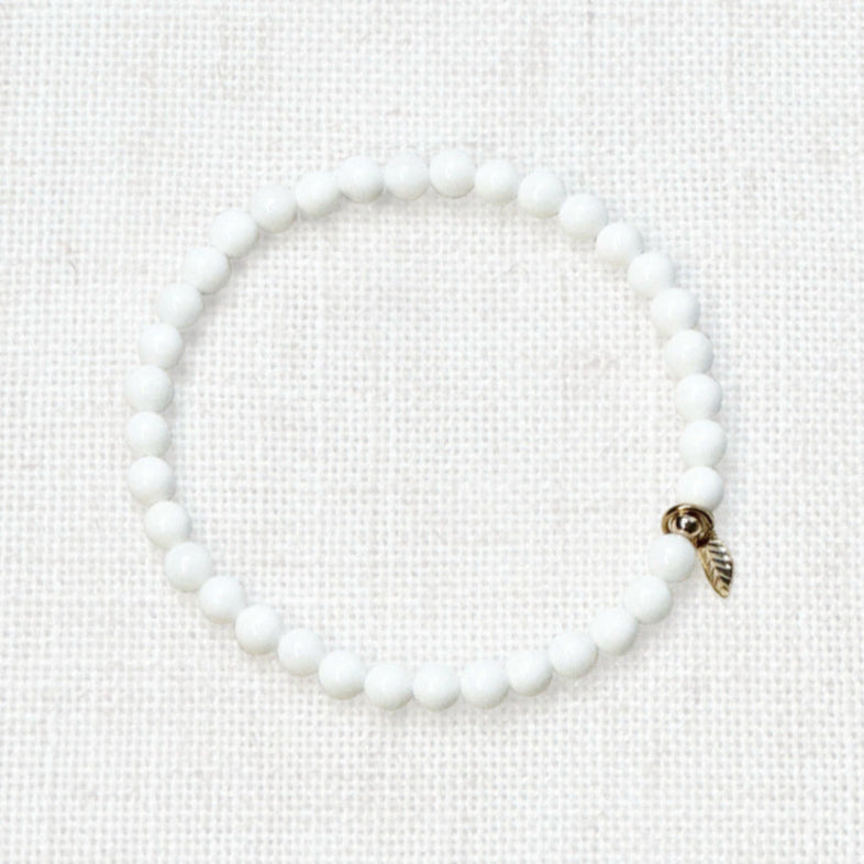 White shell bracelet 4mm with golden leaf charm on linen background
