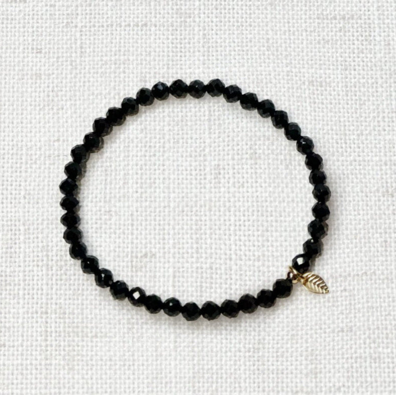 black spinel bracelet 4mm with golden leaf charm on neutral background